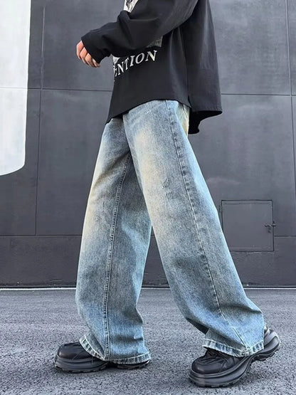 Person wearing oversized light blue jeans and black shoes against a gray wall.