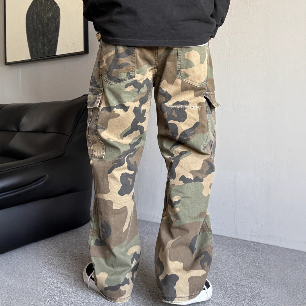 Person wearing camouflage pants in a room with a black couch and framed picture on the wall.