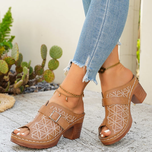 Brown open-toe shoes with geometric patterns worn with light blue jeans against a neutral background.