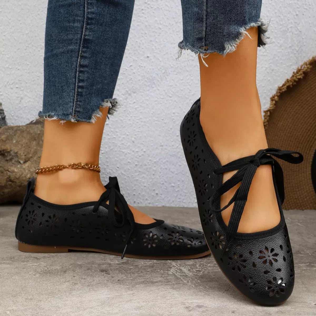 Black perforated flats worn with blue jeans on a neutral background