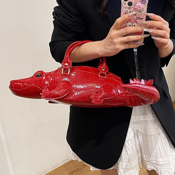 Person holding a red crocodile-shaped handbag with a neutral background