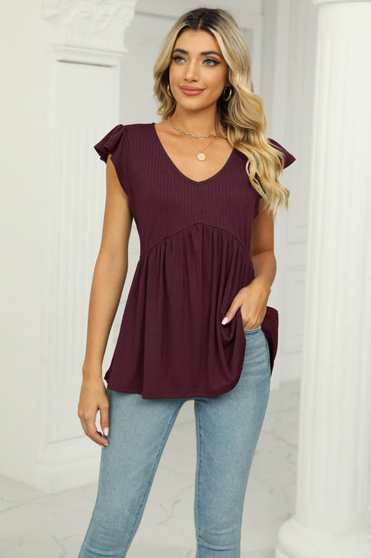 Woman wearing a burgundy top and light blue jeans in a white room.