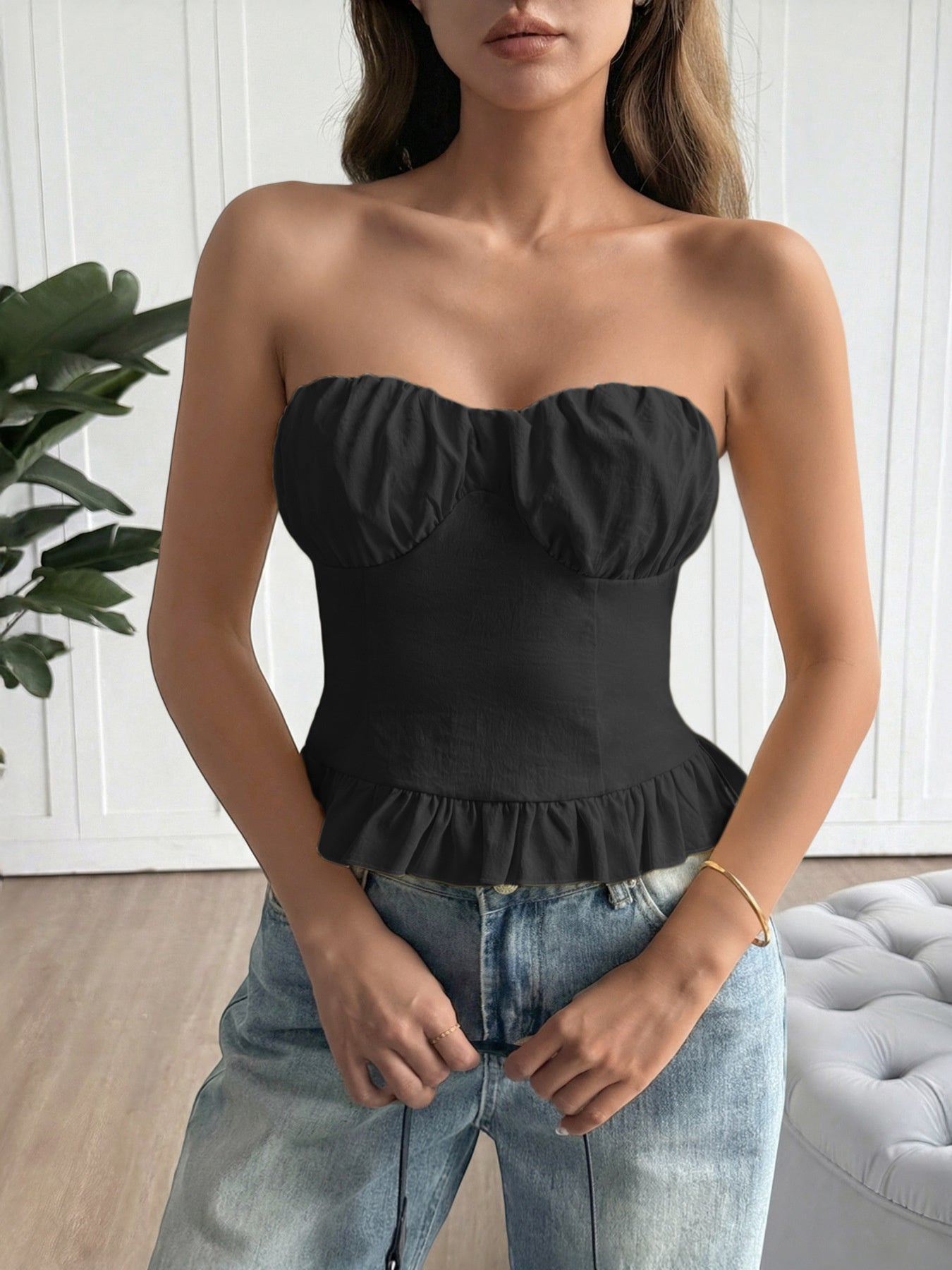 Woman wearing a black strapless top and blue jeans indoors.