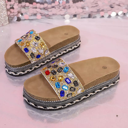 Beige sandals with colorful gemstones on a pink glittery background
