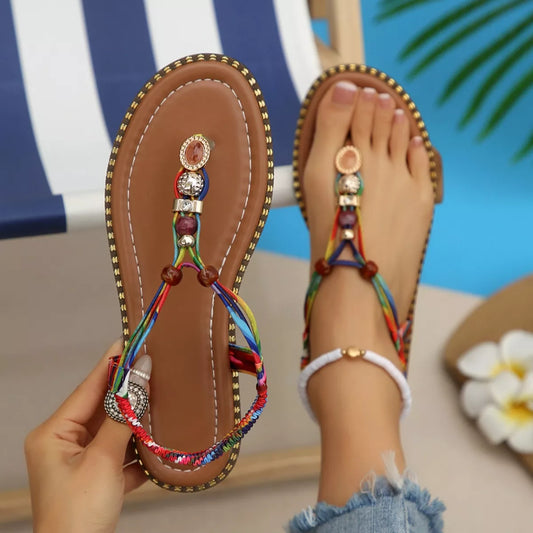 Colorful sandals with decorative straps worn by a person sitting by a pool.