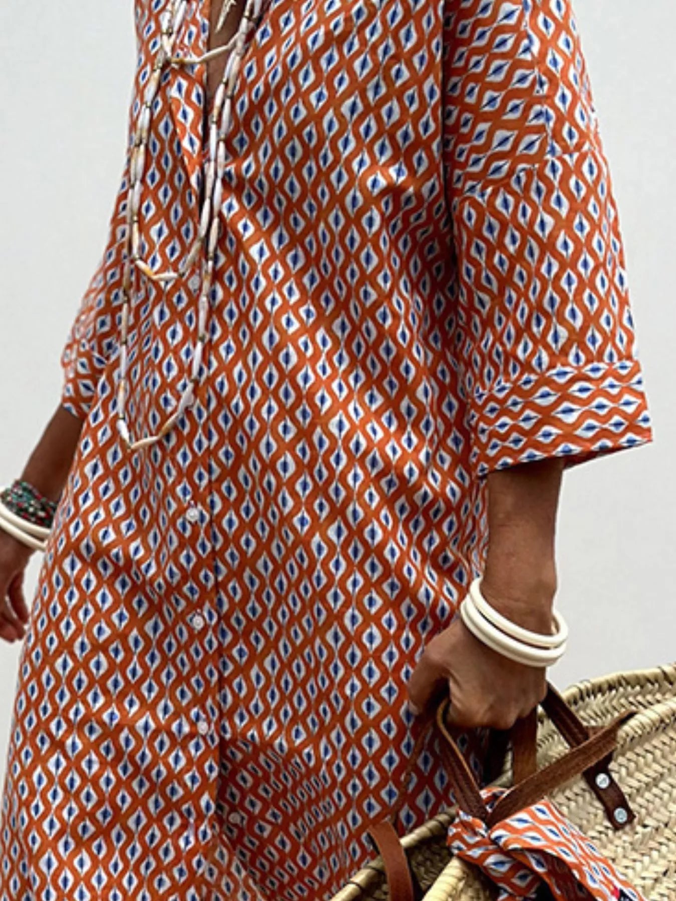 Person wearing a patterned dress holding a woven bag against a neutral background