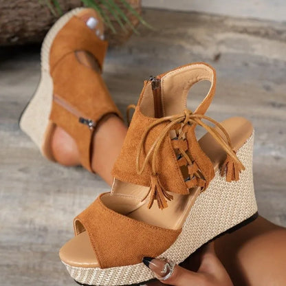 Brown wedge sandals with tassels on a wooden floor