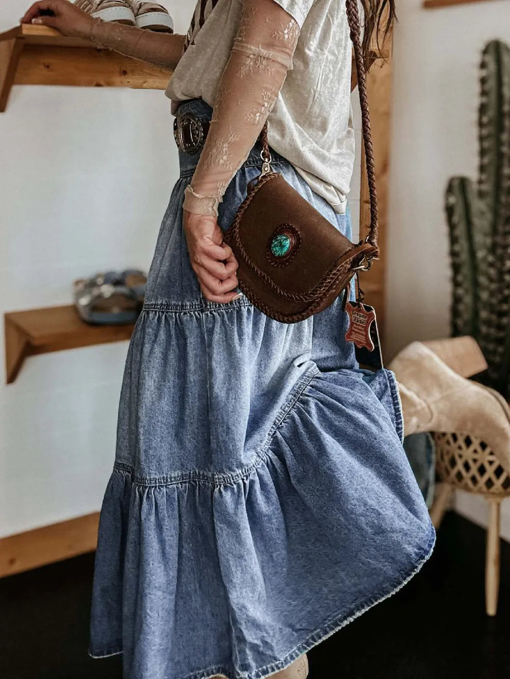 Person wearing a denim dress holding a brown leather bag with a green stone.