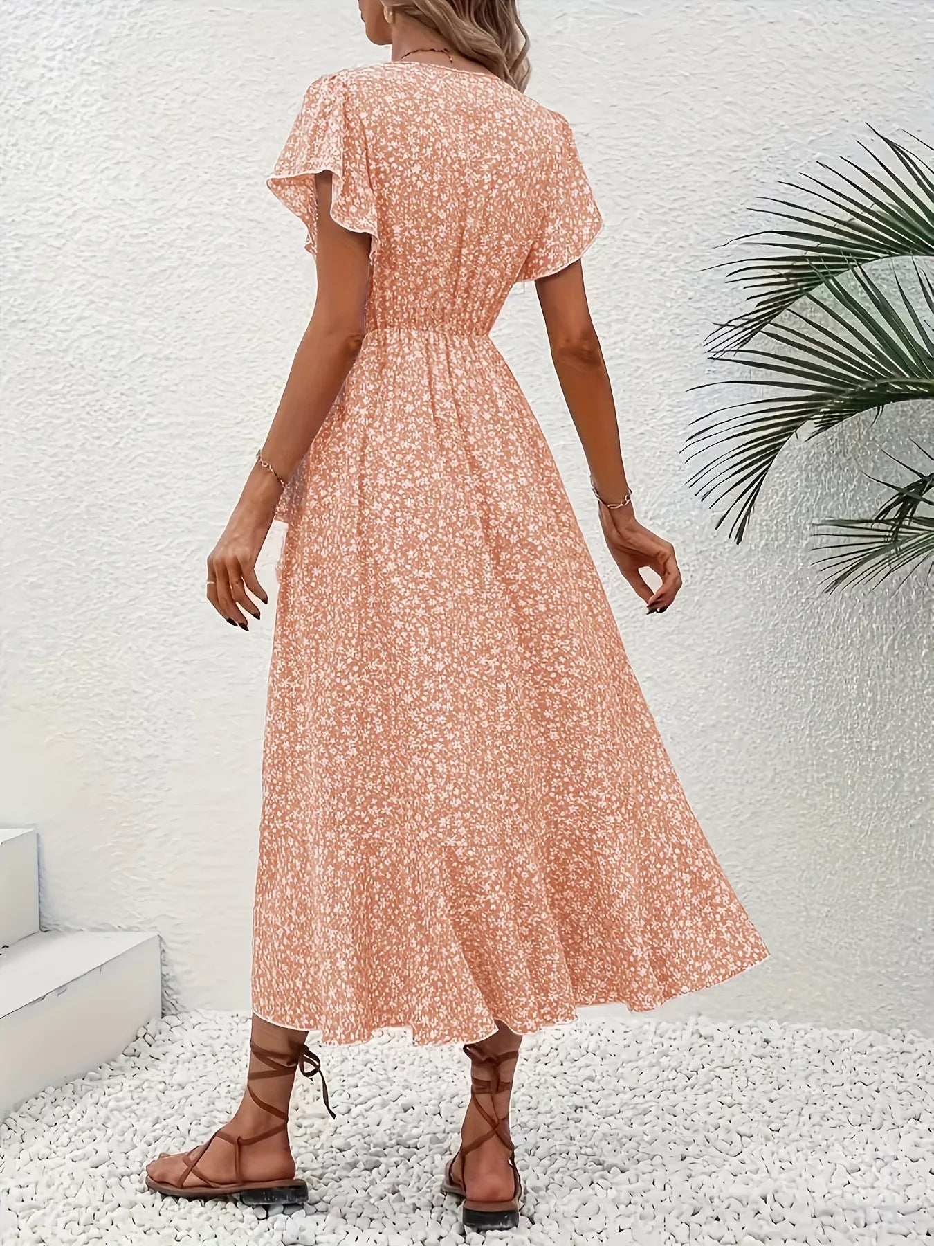 Woman wearing a floral dress standing against a white wall with a plant.