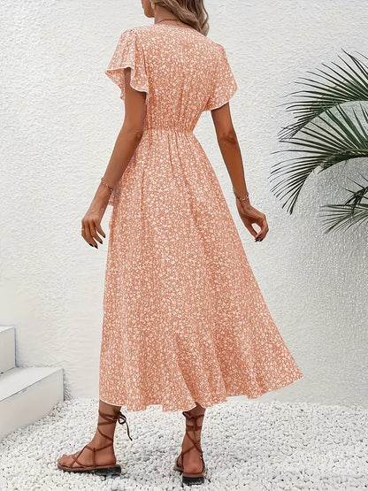 Woman wearing a floral dress standing against a white wall with a plant.
