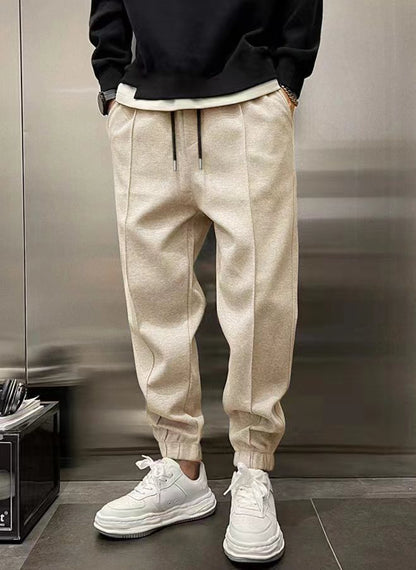 Person wearing beige jogger pants and white sneakers in a modern interior setting