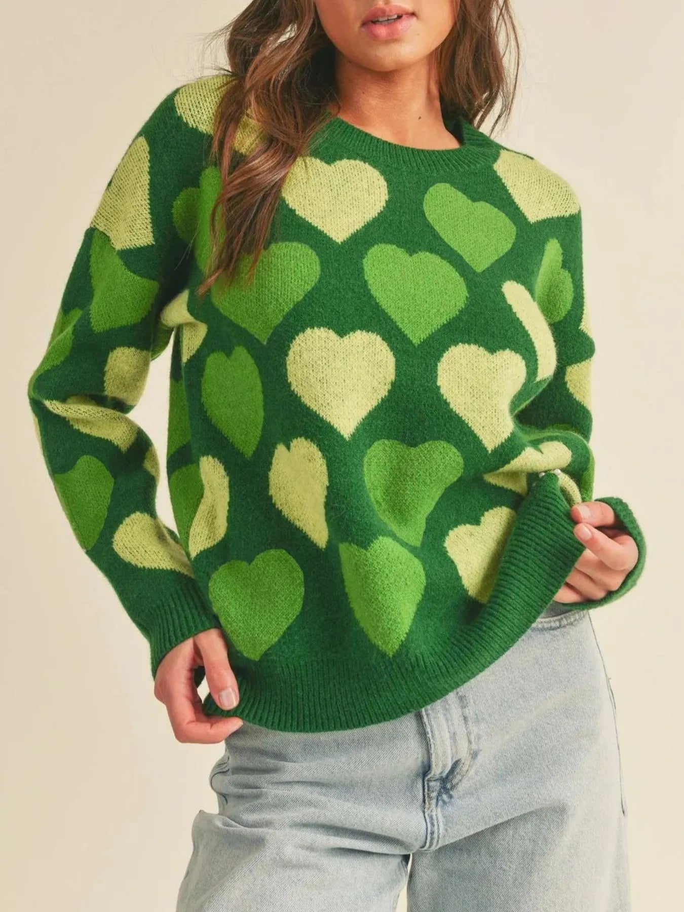 Person wearing a green sweater with heart patterns on a beige background