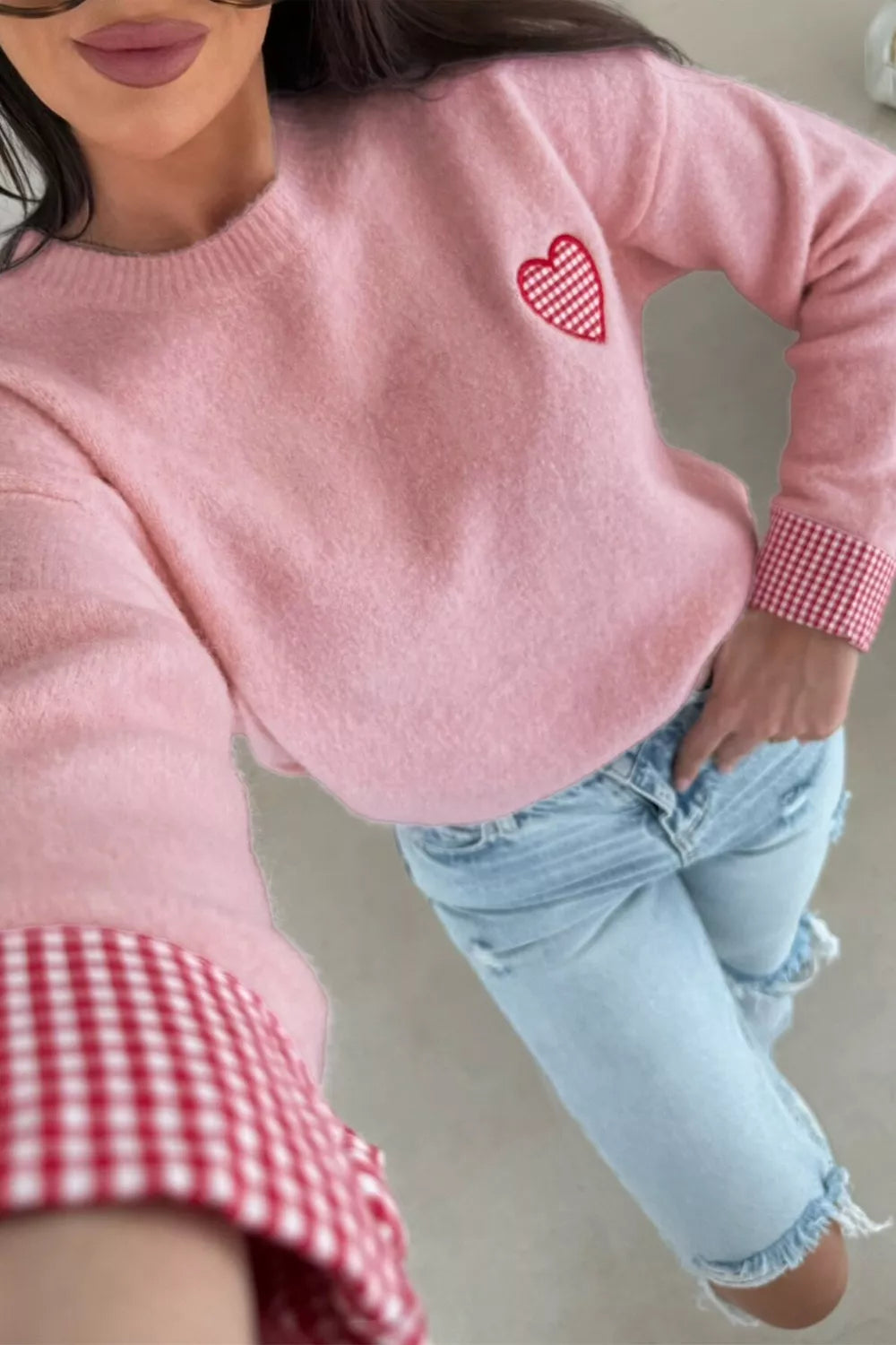 Person wearing a pink sweater with a heart design and light blue jeans.