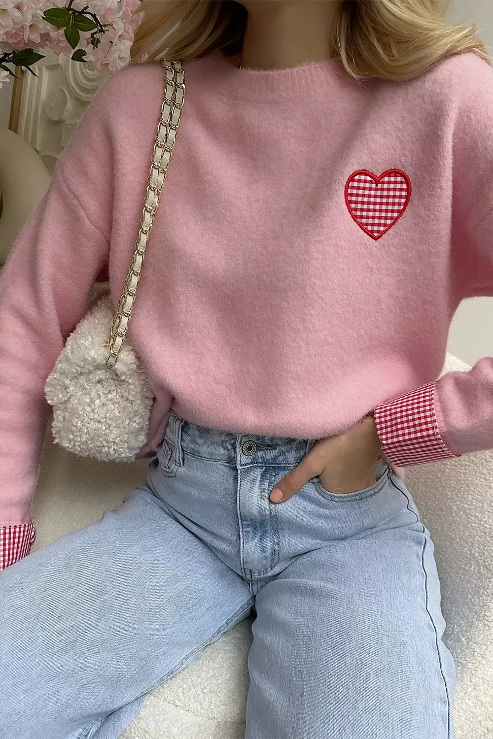 Person wearing a pink sweater with a red heart design, holding a small white bag.