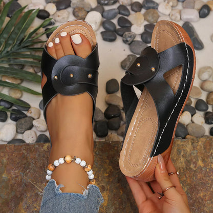 Black sandals with tan soles held by a hand against a stone background