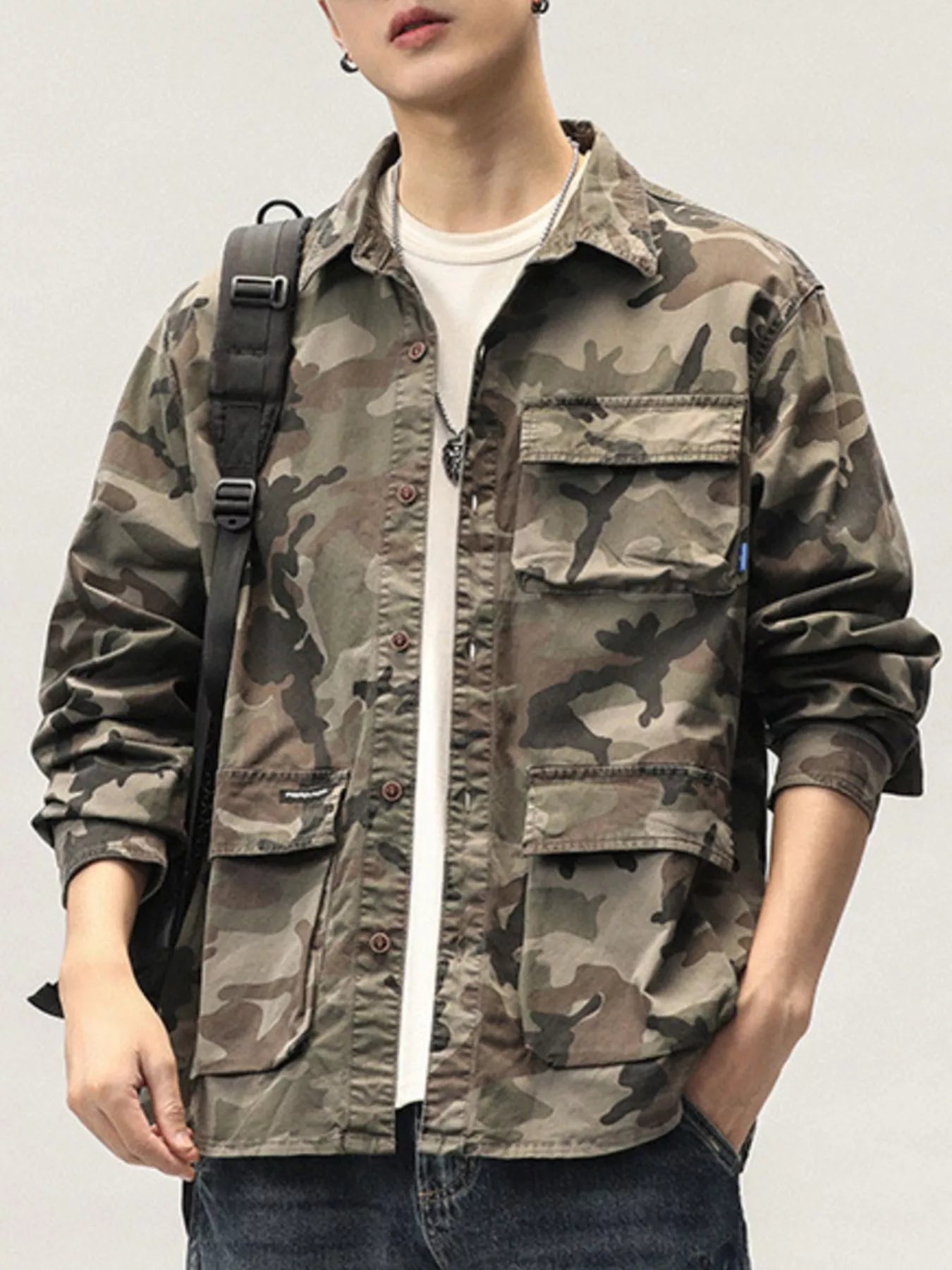Person wearing a camouflage jacket with a backpack on a plain background