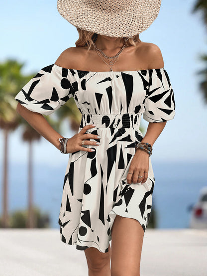 Person wearing a black and white patterned dress with a straw hat on a beach.