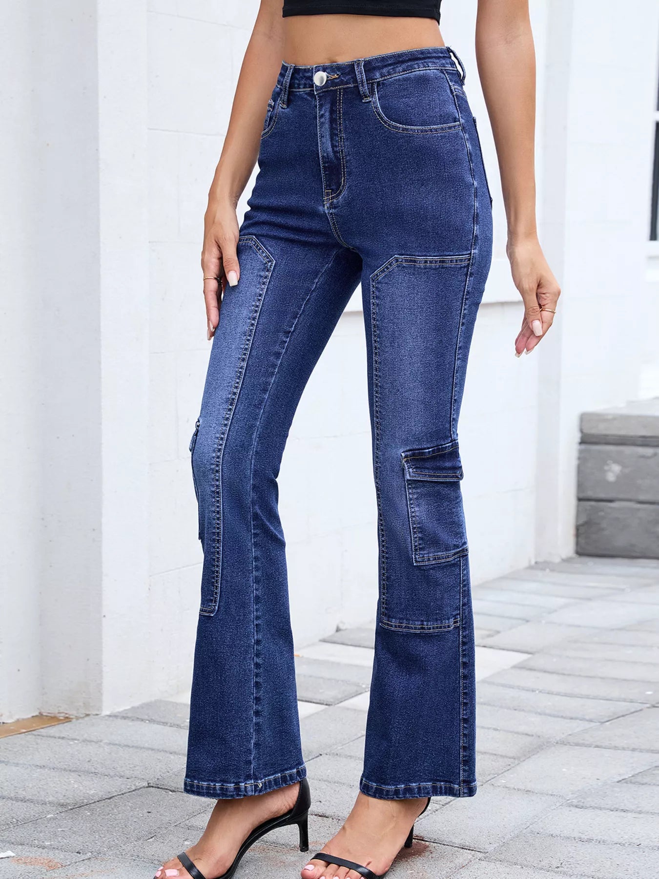 Person wearing blue flared jeans standing on a stone floor with a white wall background