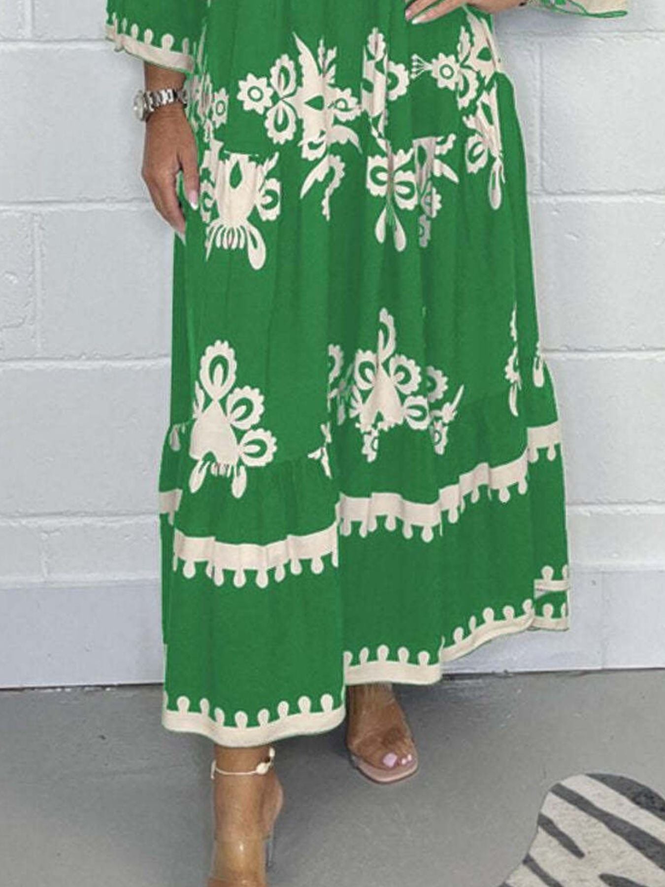 Green dress with white floral patterns worn by a person against a white brick wall.