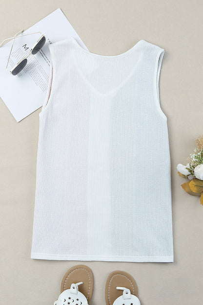 White ribbed tank top on a beige surface with sunglasses and sandals.