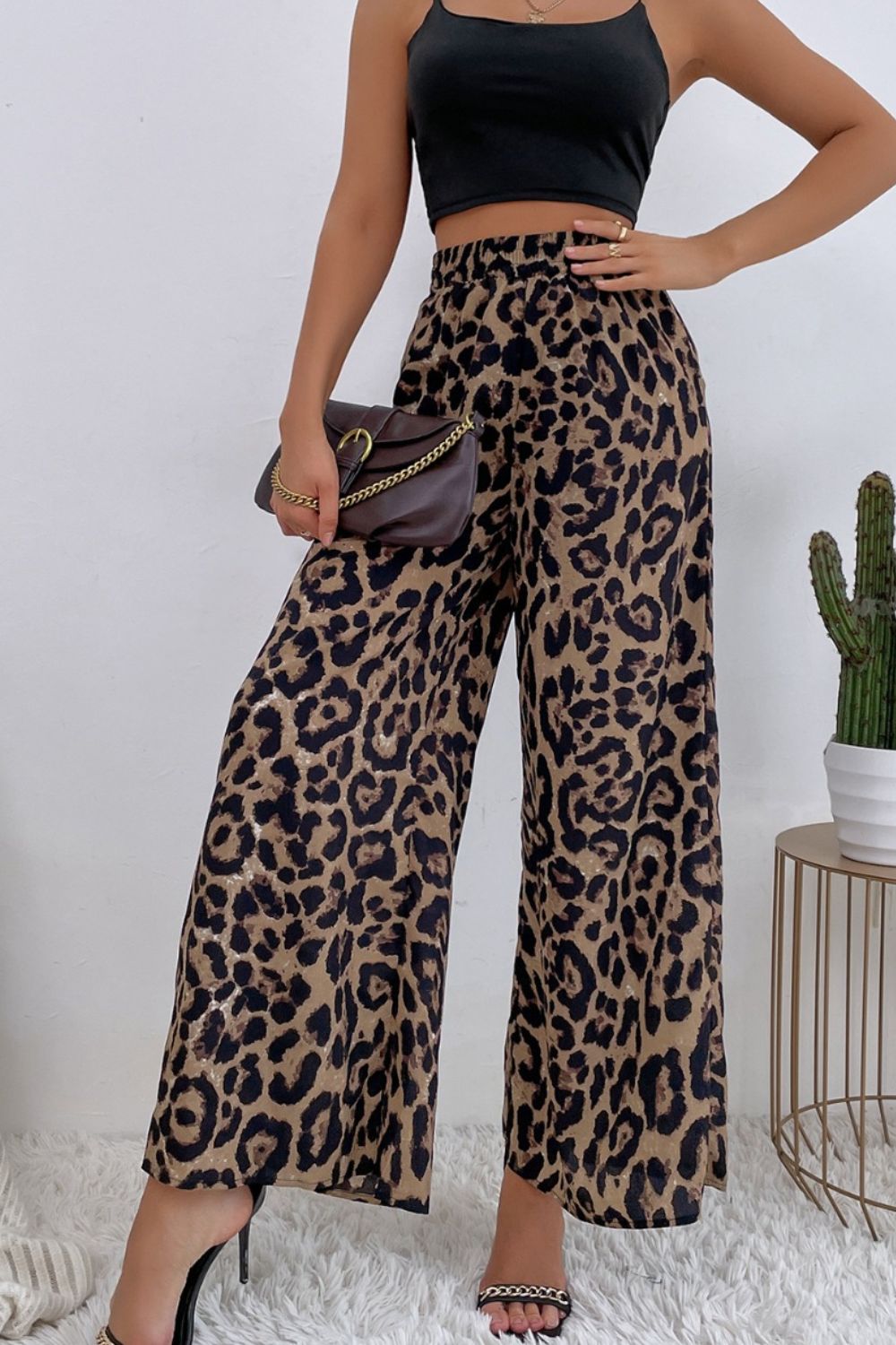 Person wearing leopard print pants and a black top, holding a small handbag.