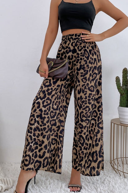 Person wearing leopard print pants and a black top, holding a small handbag.