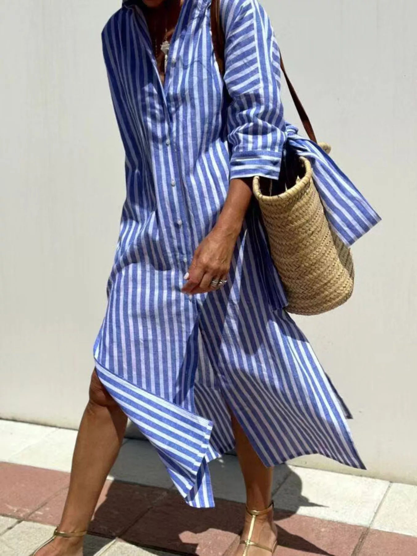 Person wearing a blue and white striped dress holding a straw bag against a plain background