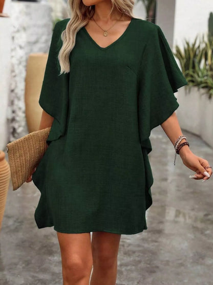 Woman wearing a green dress holding a woven bag outdoors.