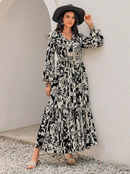 Woman wearing a black and white patterned dress with a wide-brimmed hat against a white wall.