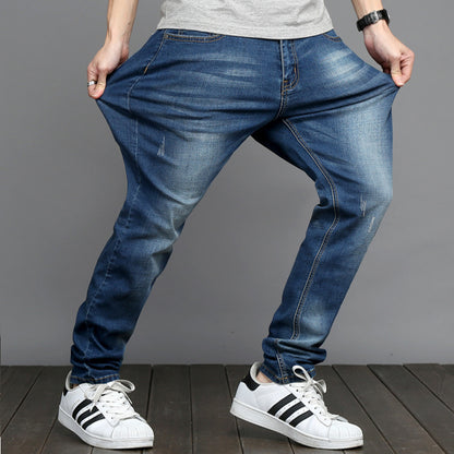 Person wearing blue jeans and white sneakers on a wooden floor with a gray background