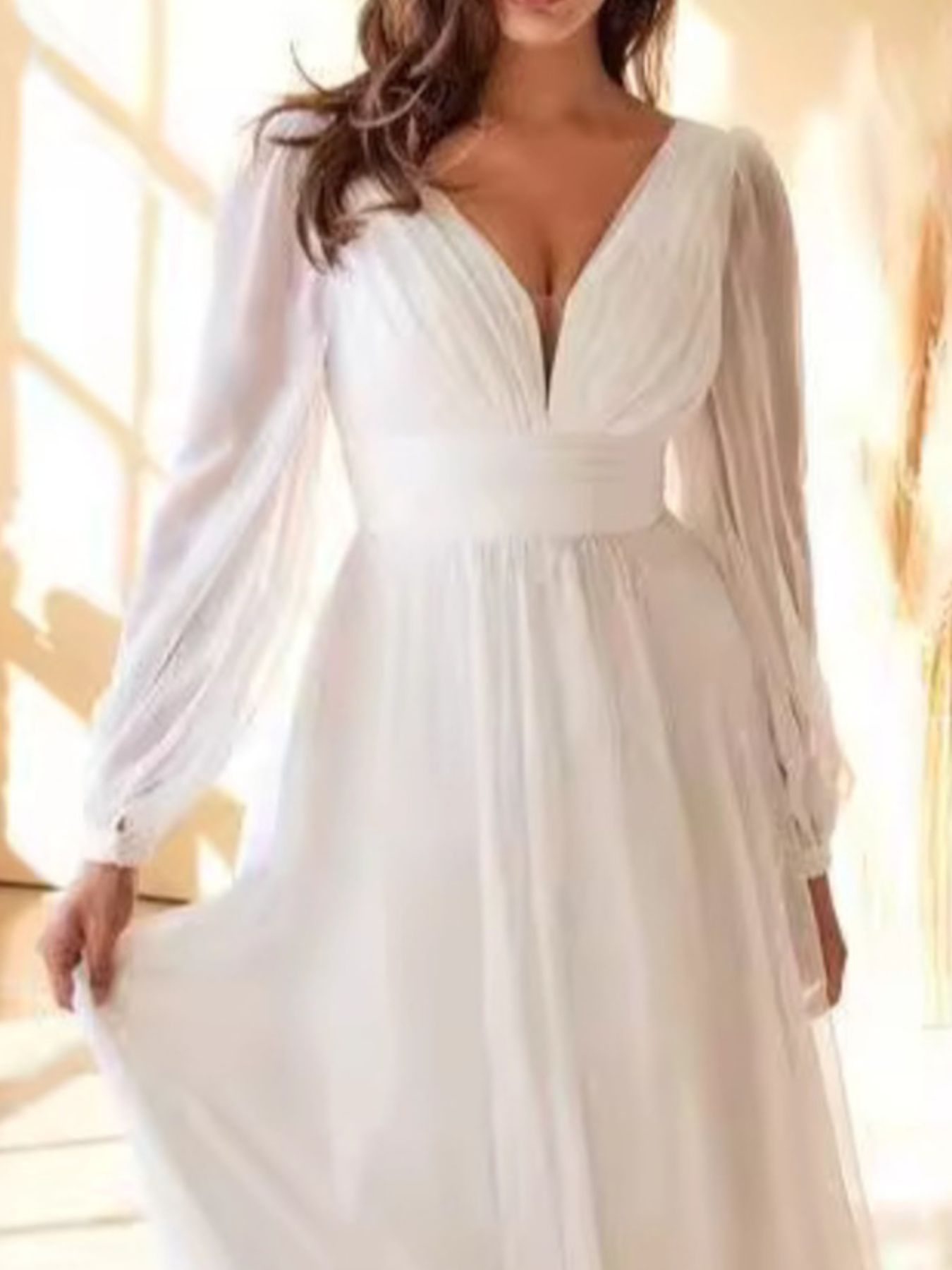White dress with long sleeves and a deep neckline on a blurred background