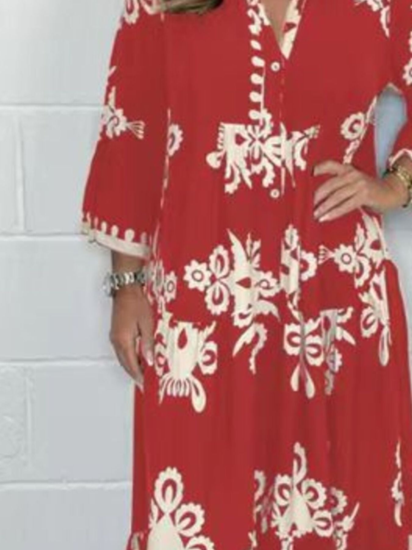 Red dress with white floral patterns worn by a person against a white brick wall.