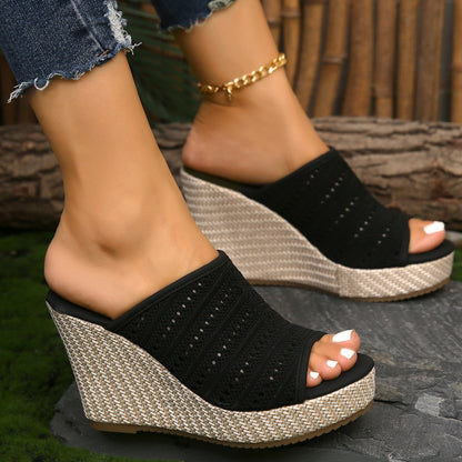 Black wedge sandals with textured sole worn by a person on a stone surface.