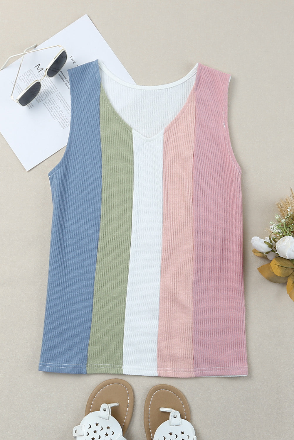 Three ribbed tank tops in blue, white, and pink on a beige surface with sunglasses and sandals.