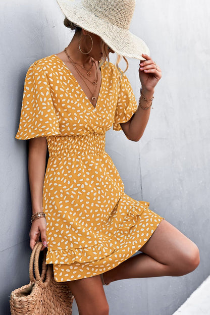 Woman wearing a yellow patterned dress and straw hat against a gray background