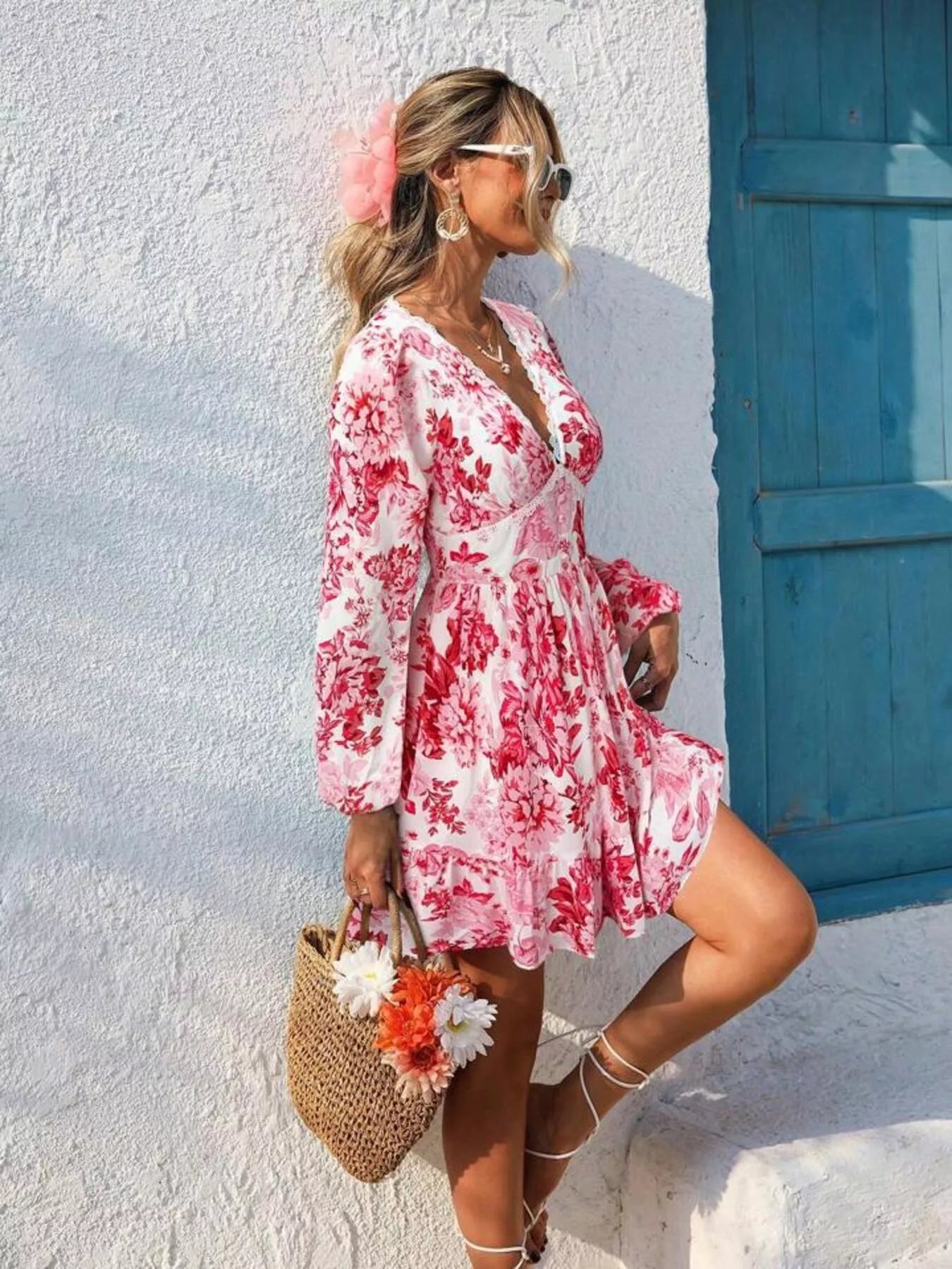 Woman in a pink floral dress standing against a white wall with a blue door.