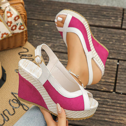 Pink and white wedge sandals with a straw sole on a wooden floor.