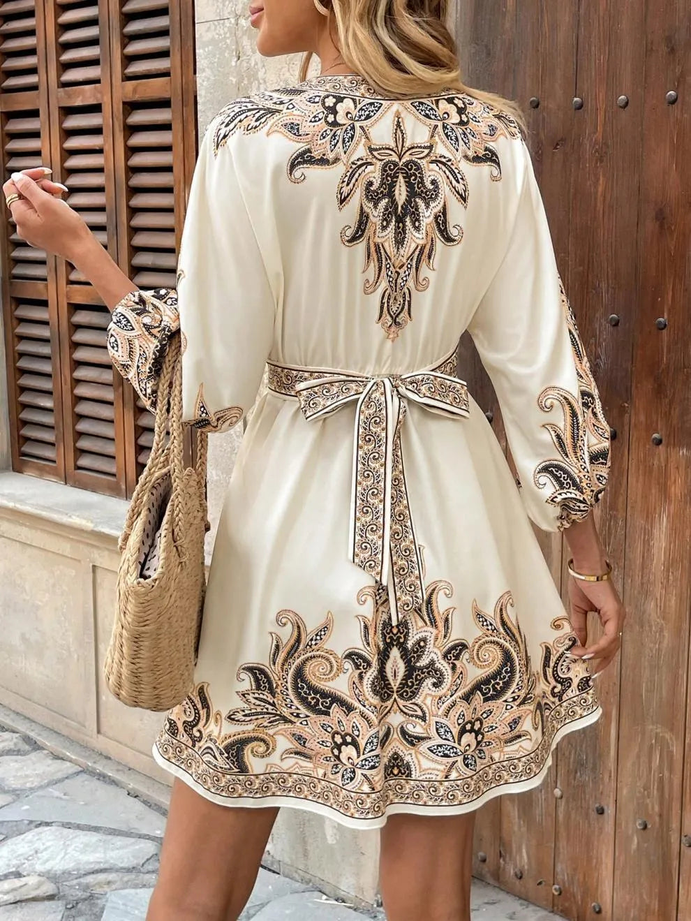 Woman wearing a white dress with intricate black and gold embroidery in an outdoor setting.