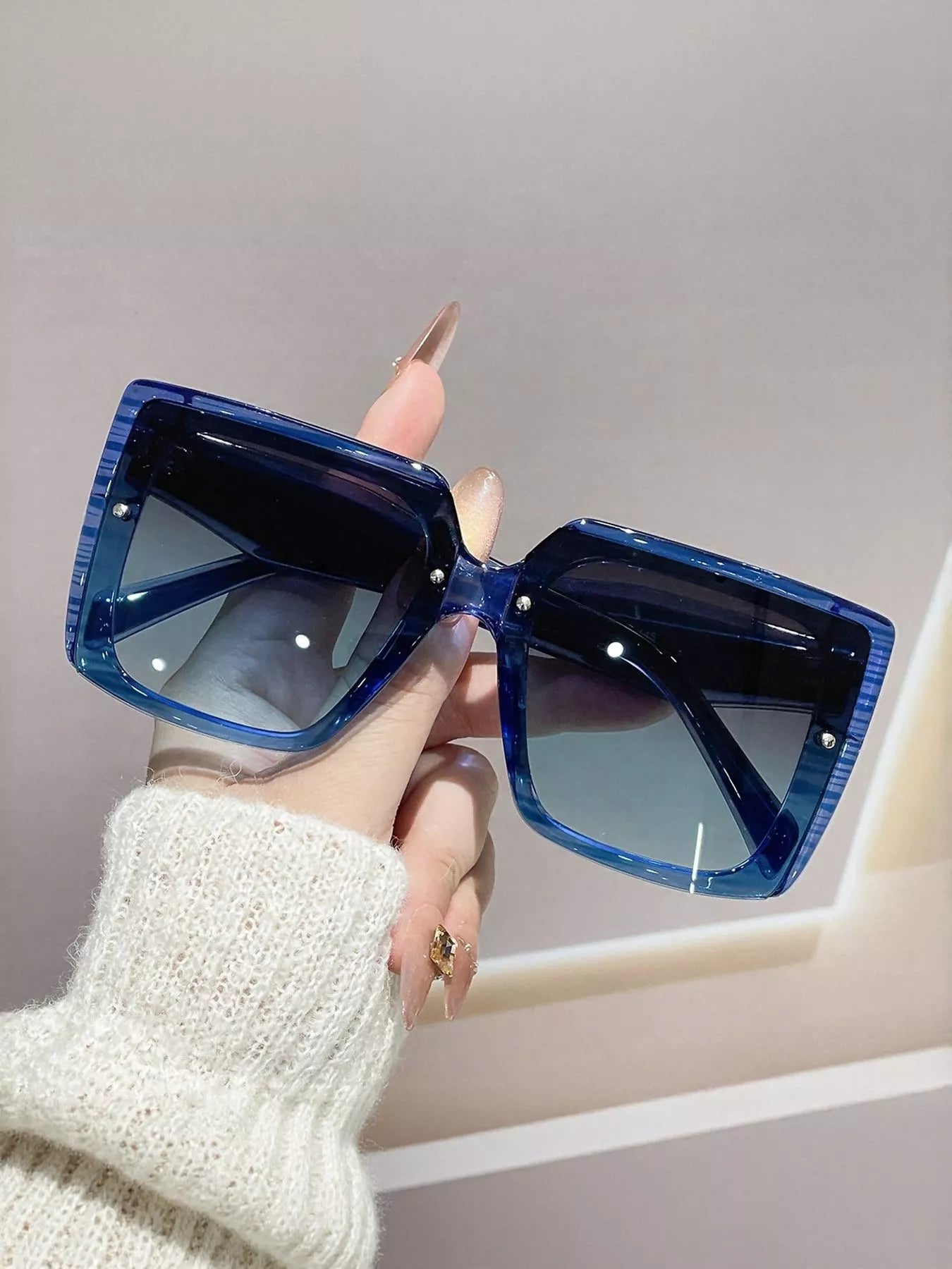 Blue sunglasses held by a hand against a neutral background