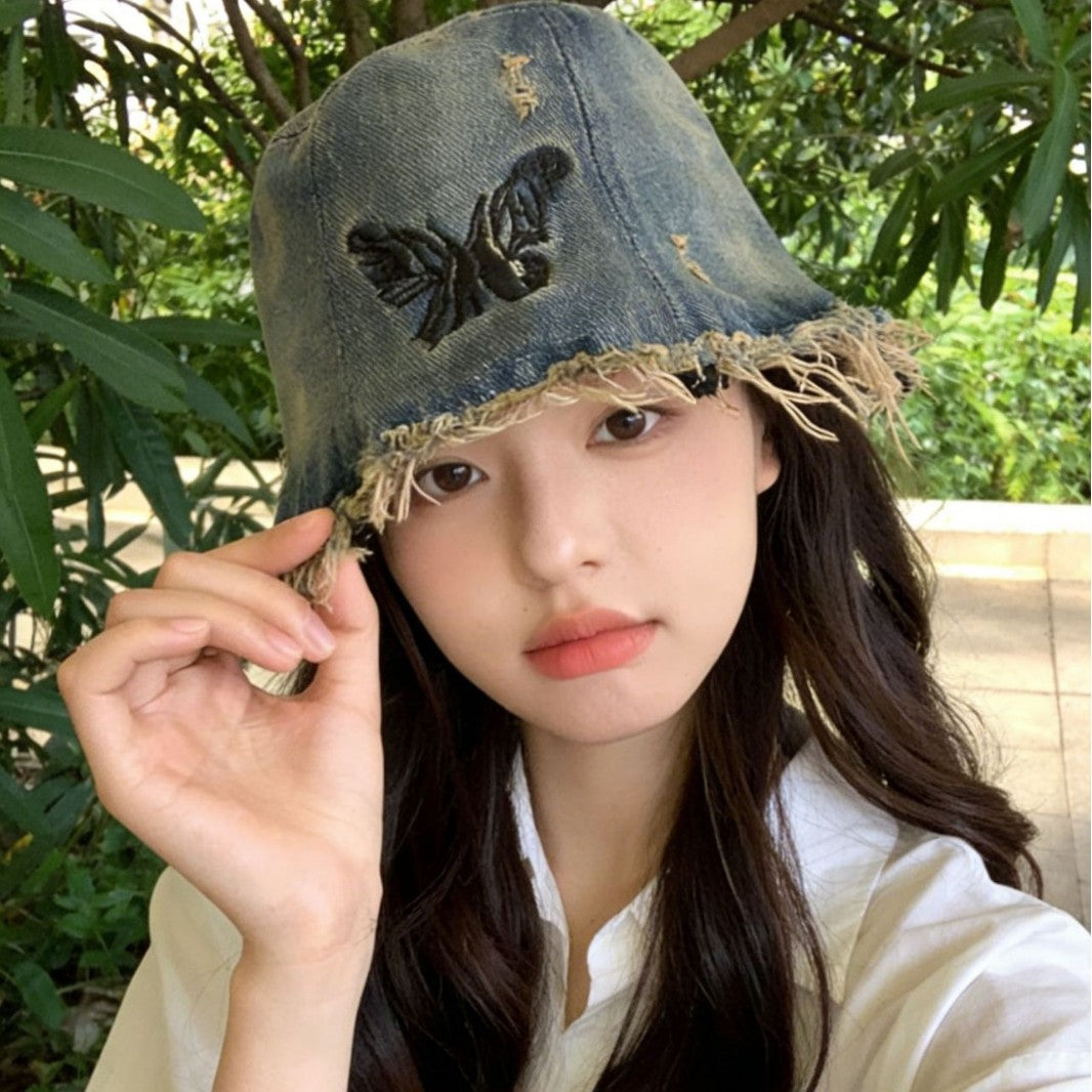 Woman wearing a denim bucket hat with a butterfly design outdoors.
