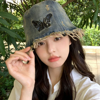 Woman wearing a denim bucket hat with a butterfly design outdoors.