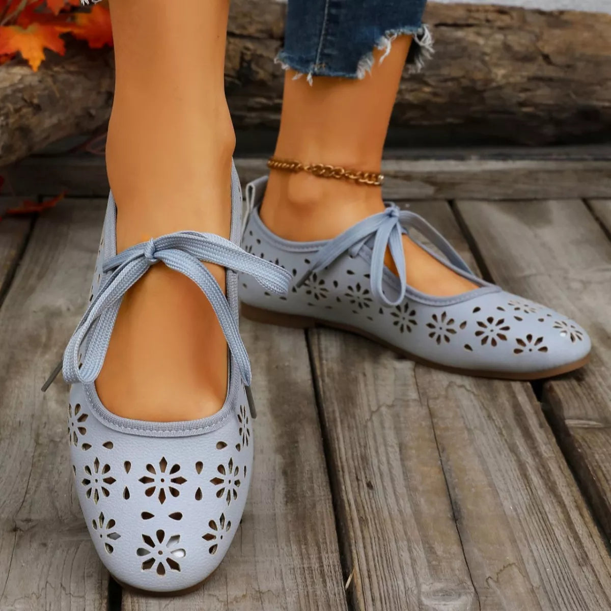 Blue perforated shoes with lace-up design worn by a person on a stone surface.