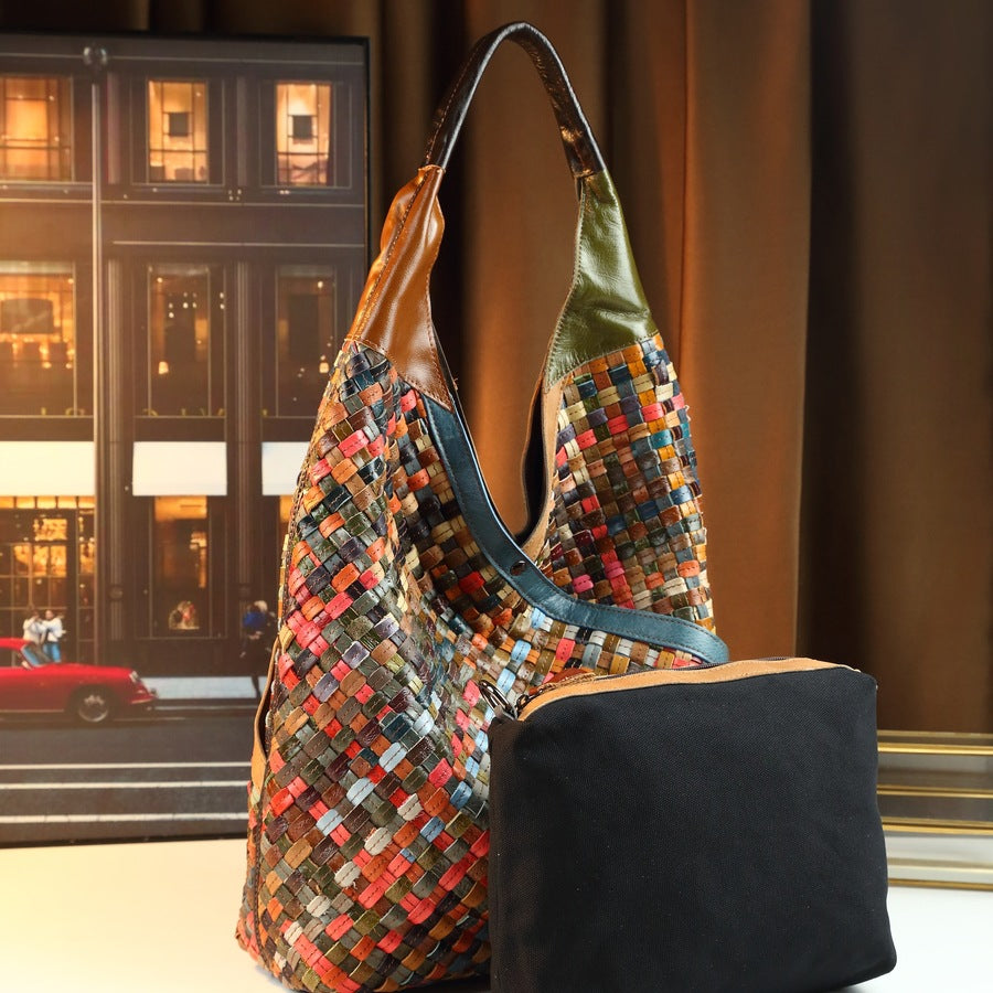 Multicolored woven handbag and black zippered pouch against a blurred city street background