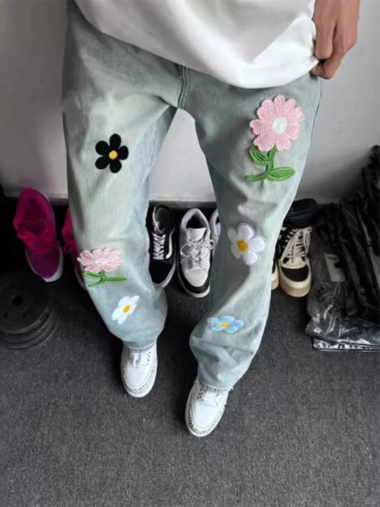 Light blue jeans with floral patches worn by a person, standing on a carpeted floor.