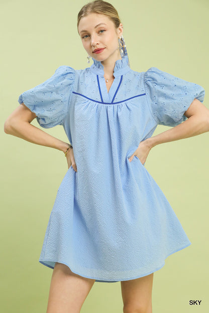 Woman wearing a light blue dress with ruffled sleeves on a green background