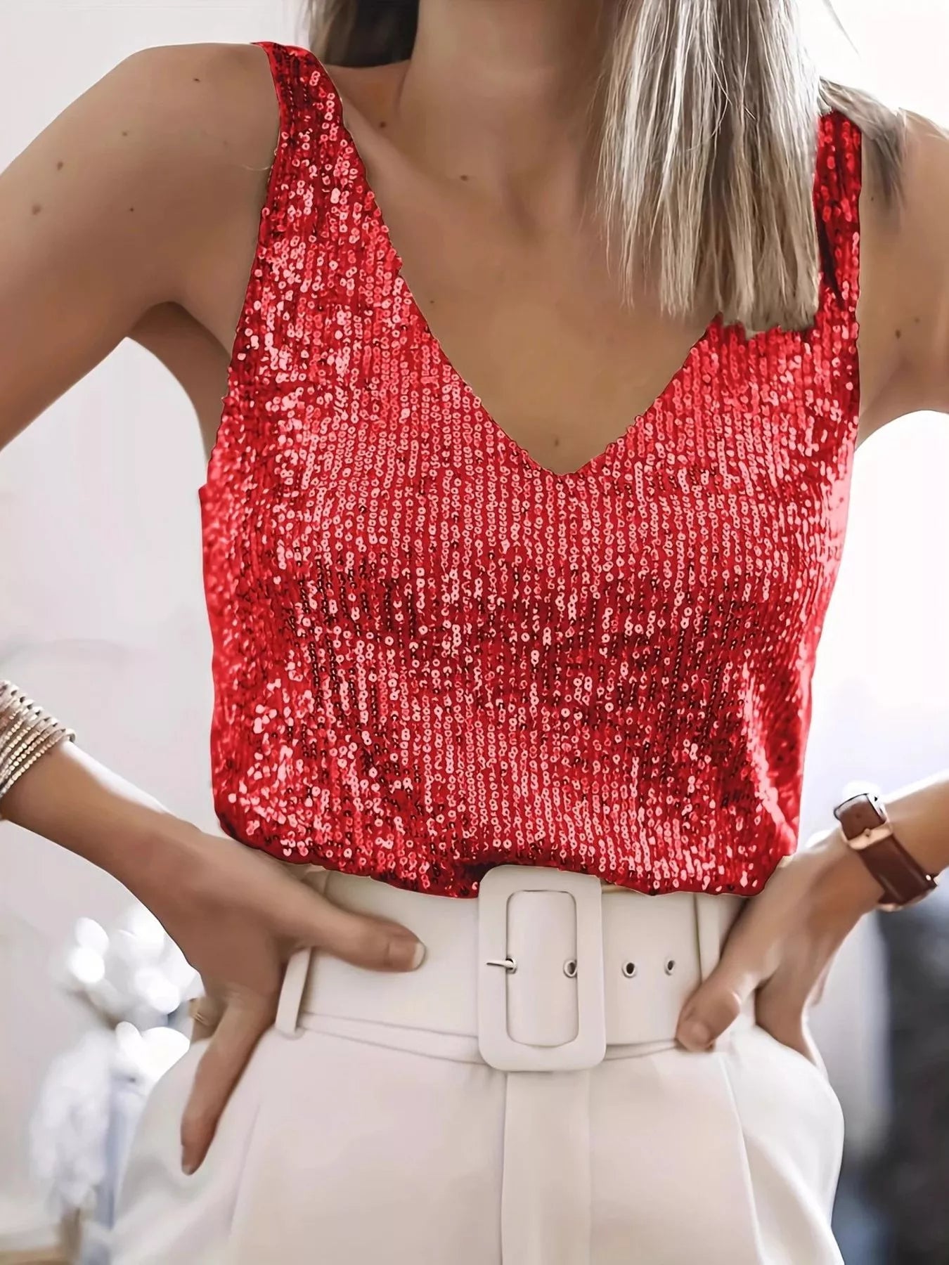Person wearing a red sequin top and beige pants with a blurred background