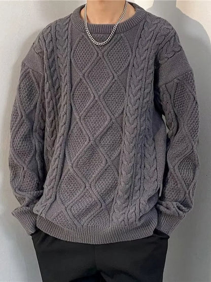 Person wearing a gray cable knit sweater against a plain background