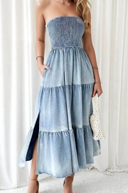 Woman wearing a strapless, tiered denim dress against a white curtain background