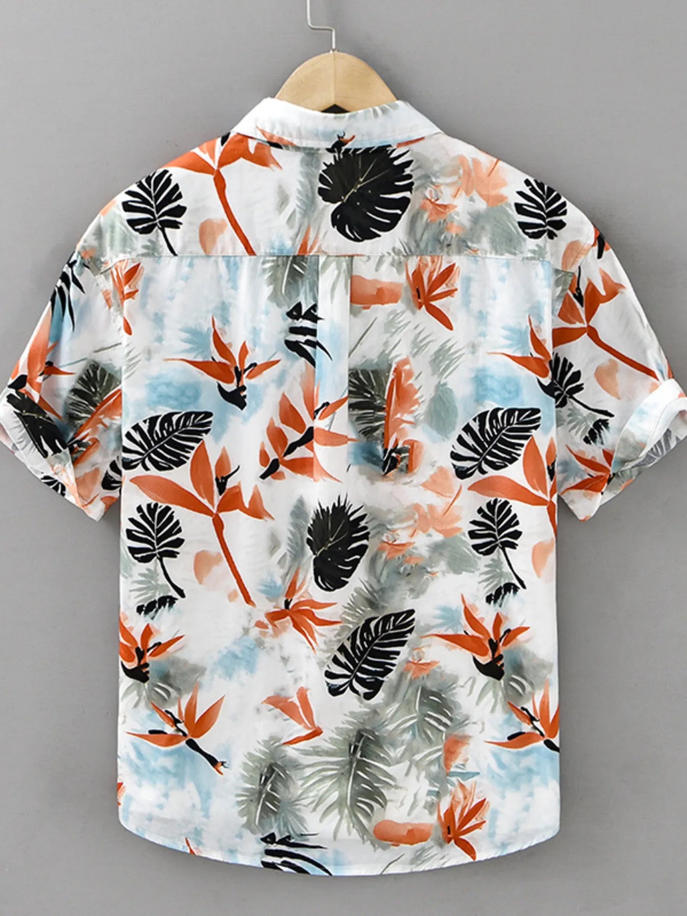 Hawaiian shirt with tropical leaf pattern on a hanger against a gray background