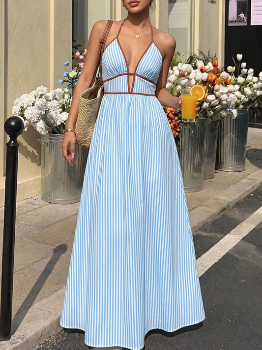 Woman in a light blue dress standing outdoors with flowers and a drink in the background